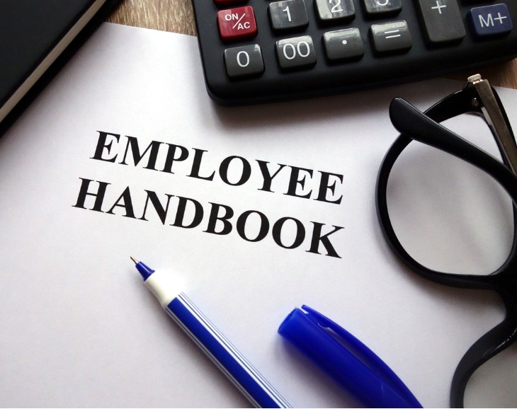 Employee handbook written on paper with pen, glasses and calculator pictured